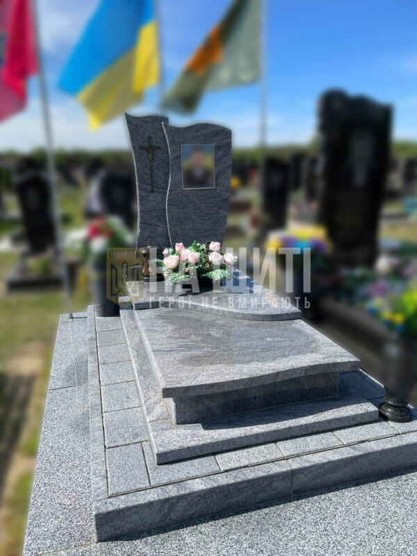 Сірий гранітний пам'ятник для військового з хвилястою стелою і квітковою композицією